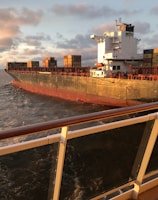 Cargo ship loaded with containers sailing across the ocean at sunset.
