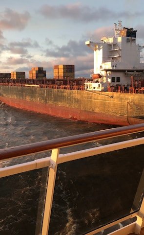 Cargo ship loaded with containers sailing across the ocean at sunset.